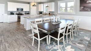 A spacious kitchen with white cabinets, a large island, and a dining area with white chairs. - Oceanfront 8 BR Beach House with a Private Pool! The Emerald (Surfside Beach)