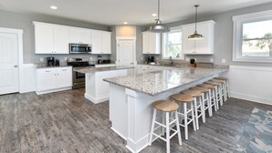 A modern kitchen with white cabinets, a granite countertop, and a bar area with stools. - Oceanfront 8 BR Beach House with a Private Pool! The Emerald (Surfside Beach)