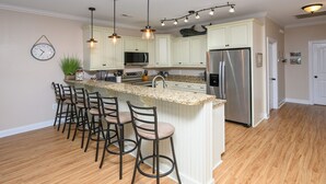 A kitchen with a central island, bar stools, stainless steel appliances, and pendant lighting. - Just a Walk to the Beach 5 BR Beach House with a Private Pool!  At Ease (Garden City)
