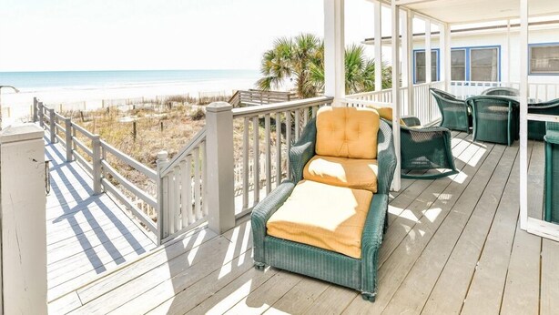 Une terrasse extérieure couverte, dotée d'une chaise en osier et d'une table, avec vue sur une plage.