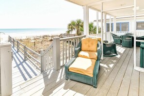 Une terrasse extérieure couverte, dotée d'une chaise en osier et d'une table, avec vue sur une plage.