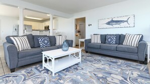 A living room with two grey sofas, a white coffee table, and a patterned rug. - Oceanfront 4 BR Beach House with Shared Pool! Portofino II 313B. (Surfside Beach)