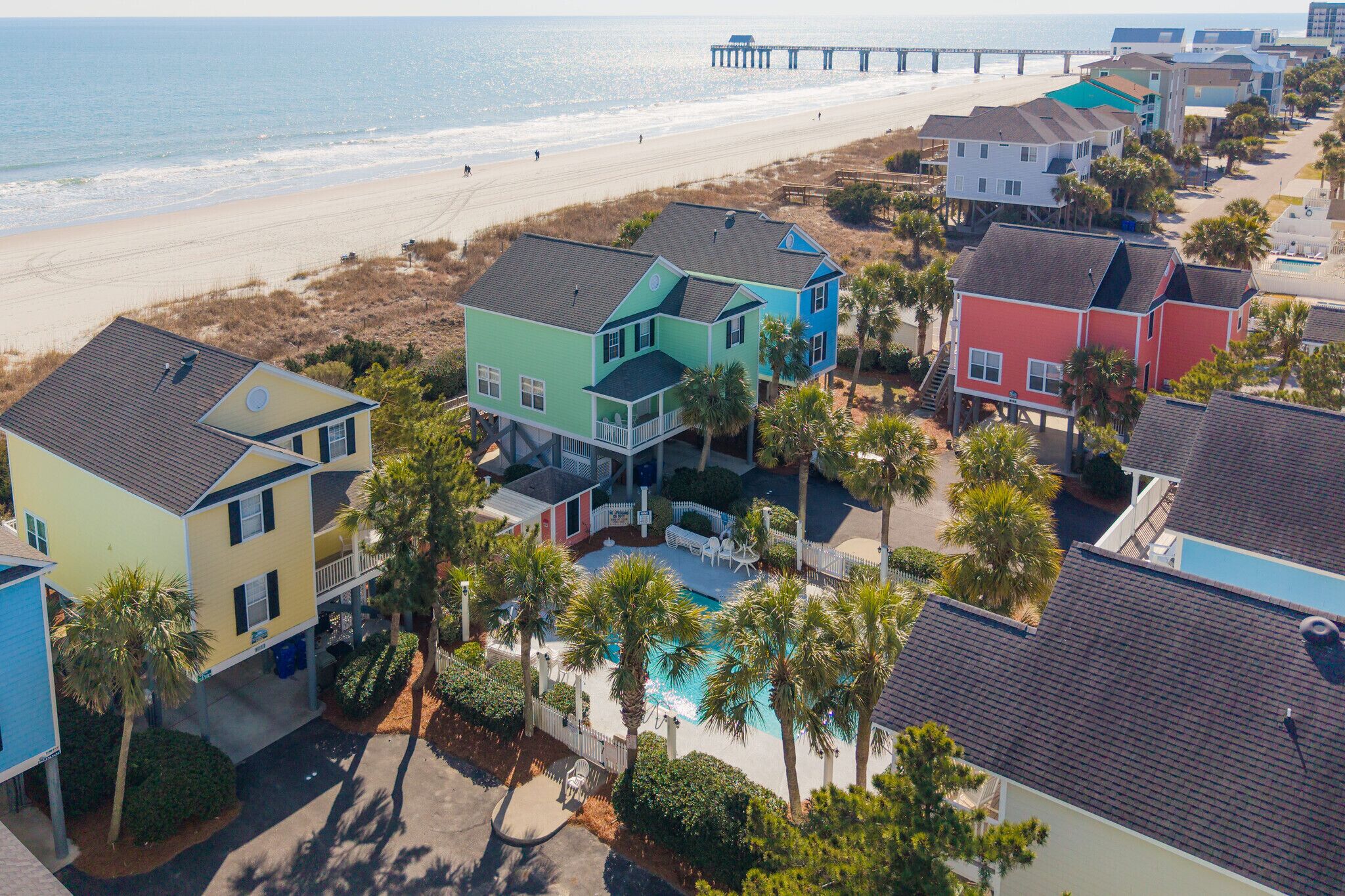 A coastal residential area with colorful houses, a beachfront, and a pier in the background.