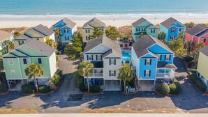 Un quartier résidentiel situé en bord de mer, avec des maisons aux couleurs vives, une vue dégagée sur l’océan et une plage de sable.