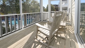 Une terrasse en bois avec un fauteuil à bascule et une porte vitrée donnant sur un espace piscine.