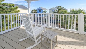 Une terrasse en bois avec une chaise berçante et une petite table, le tout entouré d’une balustrade blanche.