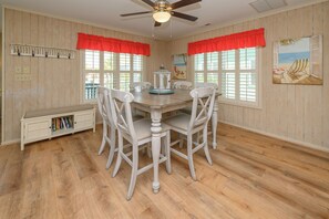 Comedor con mesa de madera, sillas blancas, ventilador de techo y estantería.