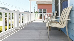 A covered porch with a white railing, a red building in the background, and two striped chairs. - 2nd Row, 3 BR Beach House with Shared Pool in Surfside Beach! Sea Bridge 1018 (Surfside Beach)