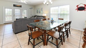 A dining area with a glass table surrounded by wooden chairs, a gray sofa, and a ceiling fan. - Pet Friendly 6 BR Beach House with a Private Pool in Surfside Beach! Sea La Vie  (Surfside Beach)