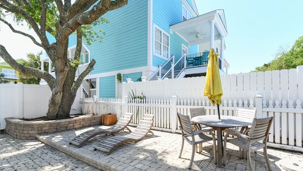 A patio with a white picket fence, a tree, and a blue house with a balcony. - Pet Friendly 6 BR Beach House with a Private Pool in Surfside Beach! Sea La Vie  (Surfside Beach)