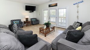 A living room with grey sofas, a wooden coffee table, a TV mounted on the wall, and a sign that reads "BEACH". - Pet Friendly 6 BR Beach House with a Private Pool in Surfside Beach! Sea La Vie  (Surfside Beach)