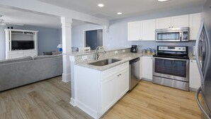 A modern kitchen with white cabinets, a granite countertop, stainless steel appliances, and a grey sofa in the living area. - Pet-Friendly Oceanfront 4 BR Beach House in Surfside Beach! Sunny Delight (Surfside Beach)