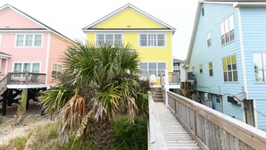 A wooden boardwalk leading to colorful houses with a palm tree in the foreground. - Pet-Friendly Oceanfront 4 BR Beach House in Surfside Beach! Sunny Delight (Surfside Beach)