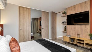 Une chambre d’hôtel moderne avec un grand lit, un téléviseur à écran plat fixé sur un mur recouvert de panneaux en bois, et une petite console en bois.