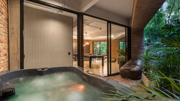Un área de spa con un jacuzzi, puertas correderas de vidrio que dan a un comedor y exuberantes plantas de interior.