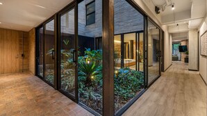 Un interior moderno con un muro de cristal que da a un jardín, suelo de madera y una zona de cocina visible.