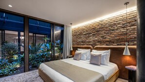 Un dormitorio moderno con una cama grande, pared de ladrillo y vista a un jardín.