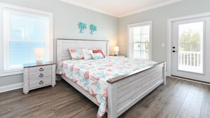Un dormitorio con cama de madera, dos mesitas de noche, una mesilla auxiliar, una ventana con persianas y una puerta con vistas al exterior.