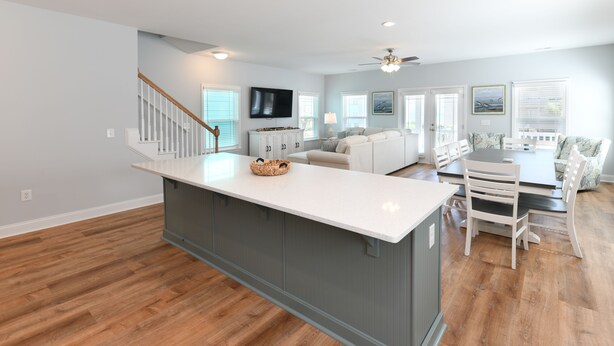 A spacious living area with a central island, a flat-screen TV mounted on the wall, and a ceiling fan. - 7 BR Beach House with a Private Pool in Surfside Beach! Salty Beaches. (Surfside Beach)