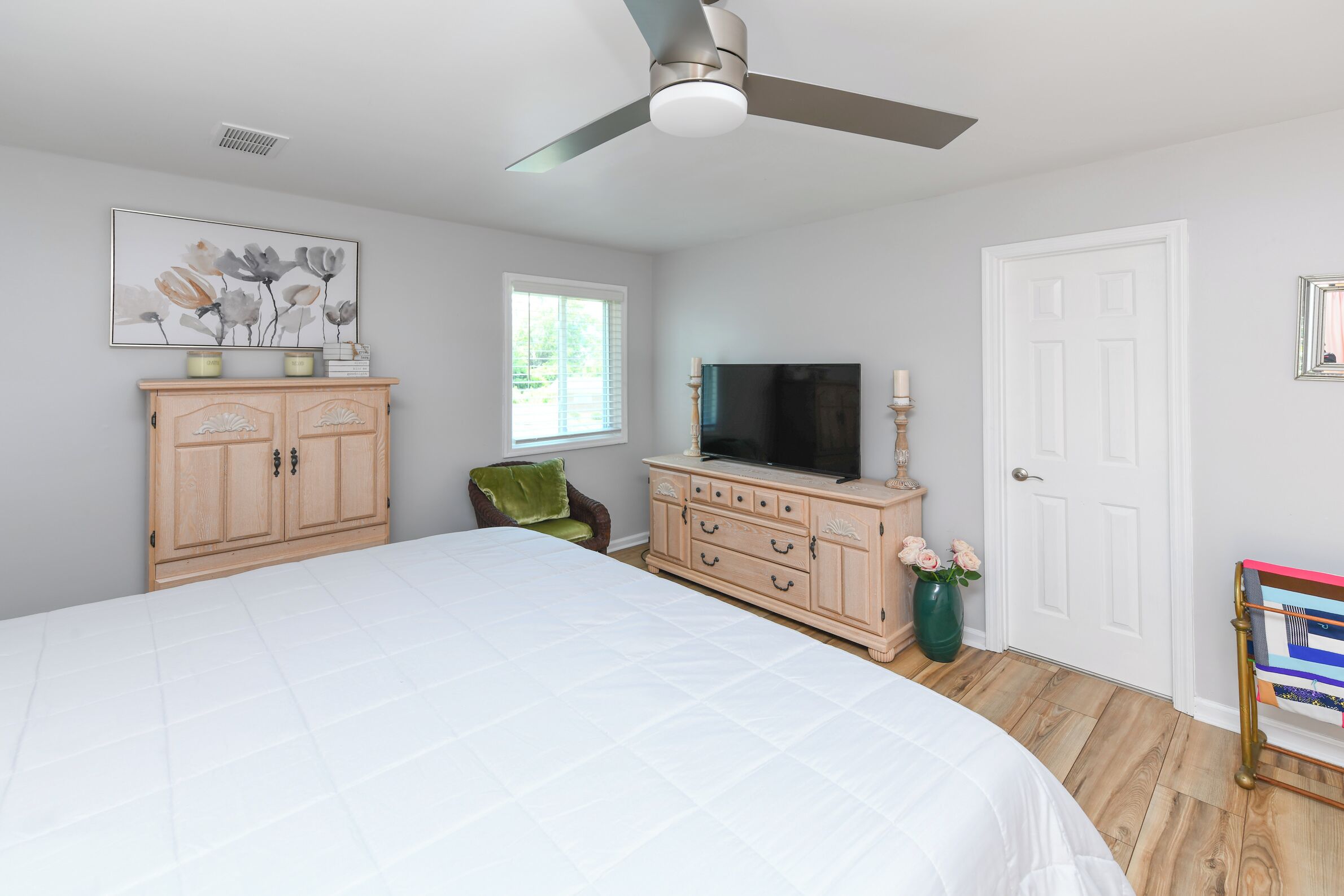 A bedroom with a large bed, a wooden dresser, a television, and a ceiling fan.
