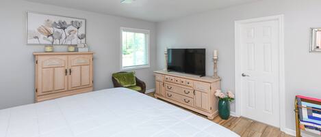 A bedroom with a large bed, a wooden dresser, a television, and a ceiling fan.