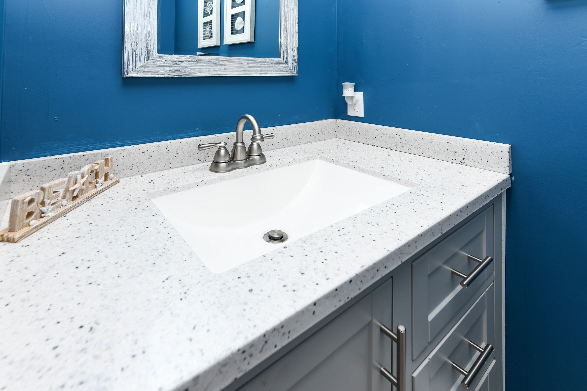 Une salle de bain avec un comptoir blanc à motifs, un seul lavabo et un miroir avec un cadre blanc.