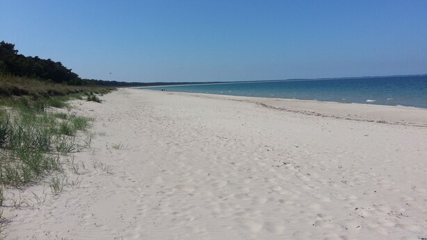 Une vaste plage de sable fin, bordée d’une eau d’un bleu limpide et d’une côte qui s’étend à perte de vue.