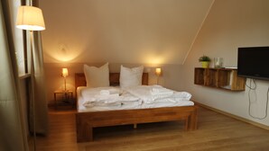 Une chambre avec un lit en bois, des lampes de chevet, un téléviseur fixé au mur et une petite étagère en bois.