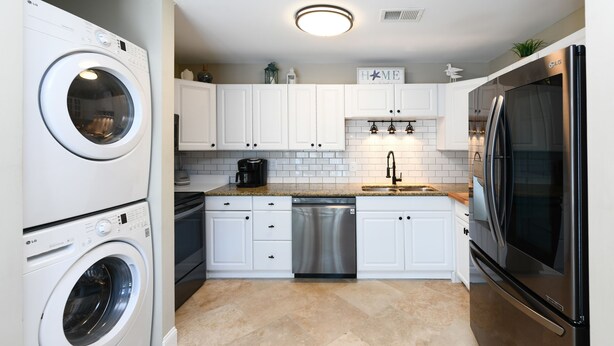 A modern kitchen with white cabinets, a stainless steel dishwasher, a washing machine, and a black refrigerator. - Walk to the Beach 3 BR Beach Condo in Surfside Beach! Family Tides (Surfside Beach)