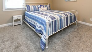 A bedroom with a bed, a nightstand, a wall clock, and a window with blinds. - Walk to the Beach 3 BR Beach Condo in Surfside Beach! Family Tides (Surfside Beach)