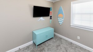 A room with a teal cabinet, a mounted TV, and a surfboard decoration on the wall. - Walk to the Beach 3 BR Beach Condo in Surfside Beach! Family Tides (Surfside Beach)