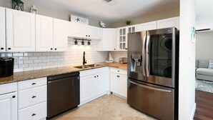 A modern kitchen with white cabinets, stainless steel appliances, and a tiled backsplash. - Walk to the Beach 3 BR Beach Condo in Surfside Beach! Family Tides (Surfside Beach)