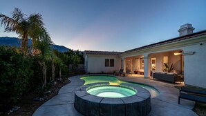 A pool area with a curved design, surrounded by a patio and a building with a tiled roof. - Paradise Palms | Pool + Spa (Palm Springs)