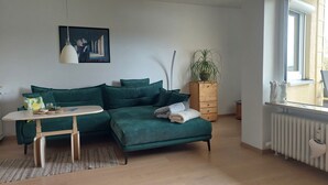 Ein modernes Wohnzimmer mit einem blaugrünen Sofa, einem kleinen runden Tisch, einer Zimmerpflanze und einer Heizung.