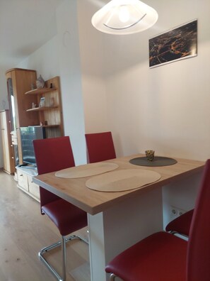 Un coin repas avec une table en bois, des chaises rouges et un luminaire fixé au mur.
