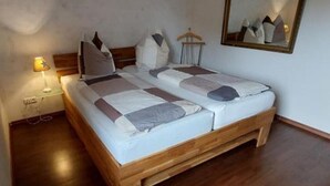 Ein ordentlich bezogenes Bett mit hölzernem Gestell, einer Nachttischlampe und einem Spiegel an der Wand.