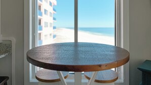Une table ronde en bois, placée devant une fenêtre offrant une vue sur la plage.