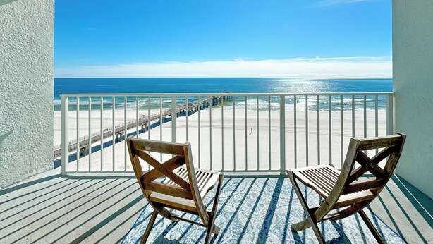 Un balcon avec deux chaises en bois donnant sur une plage et offrant une vue sur l’océan.