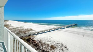 Une plage avec une jetée en bois qui s’avance dans l’océan, une plage de sable blanc et un ciel bleu clair.