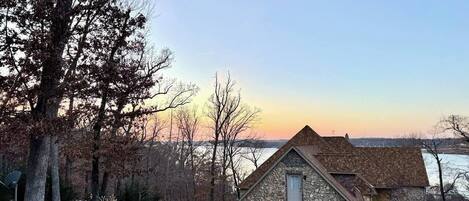 A stone house with a sloped roof, a driveway, and a view of a body of water in the background.