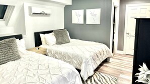 Une chambre avec deux lits, un ventilateur de plafond, un appareil de climatisation et des œuvres d’art accrochées au mur.