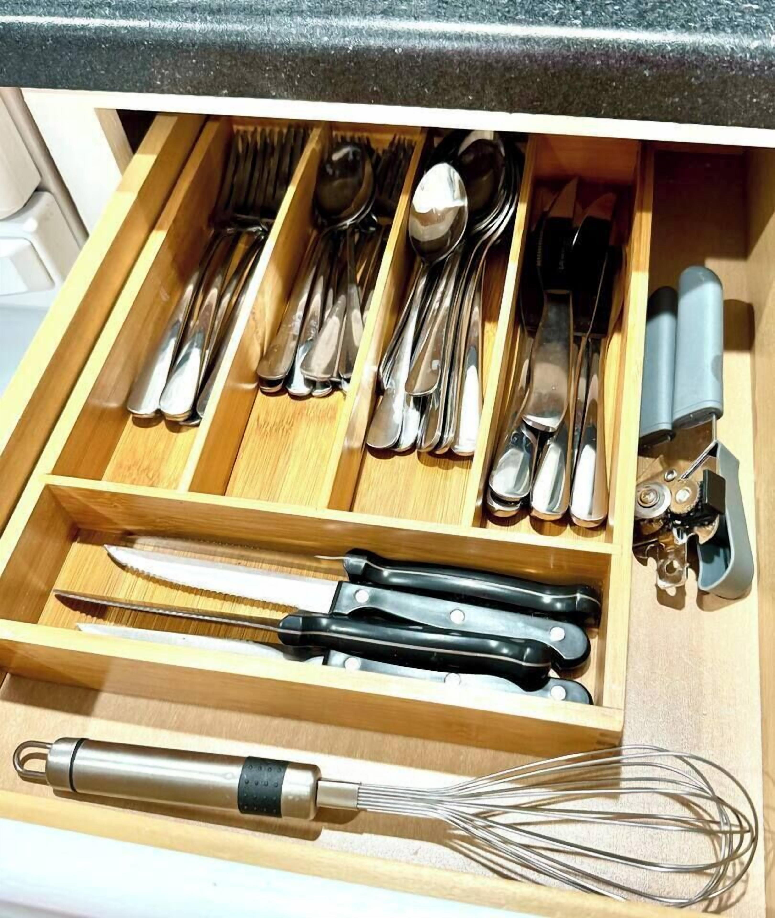 A drawer with various kitchen utensils including spoons, forks, knives, and a whisk.