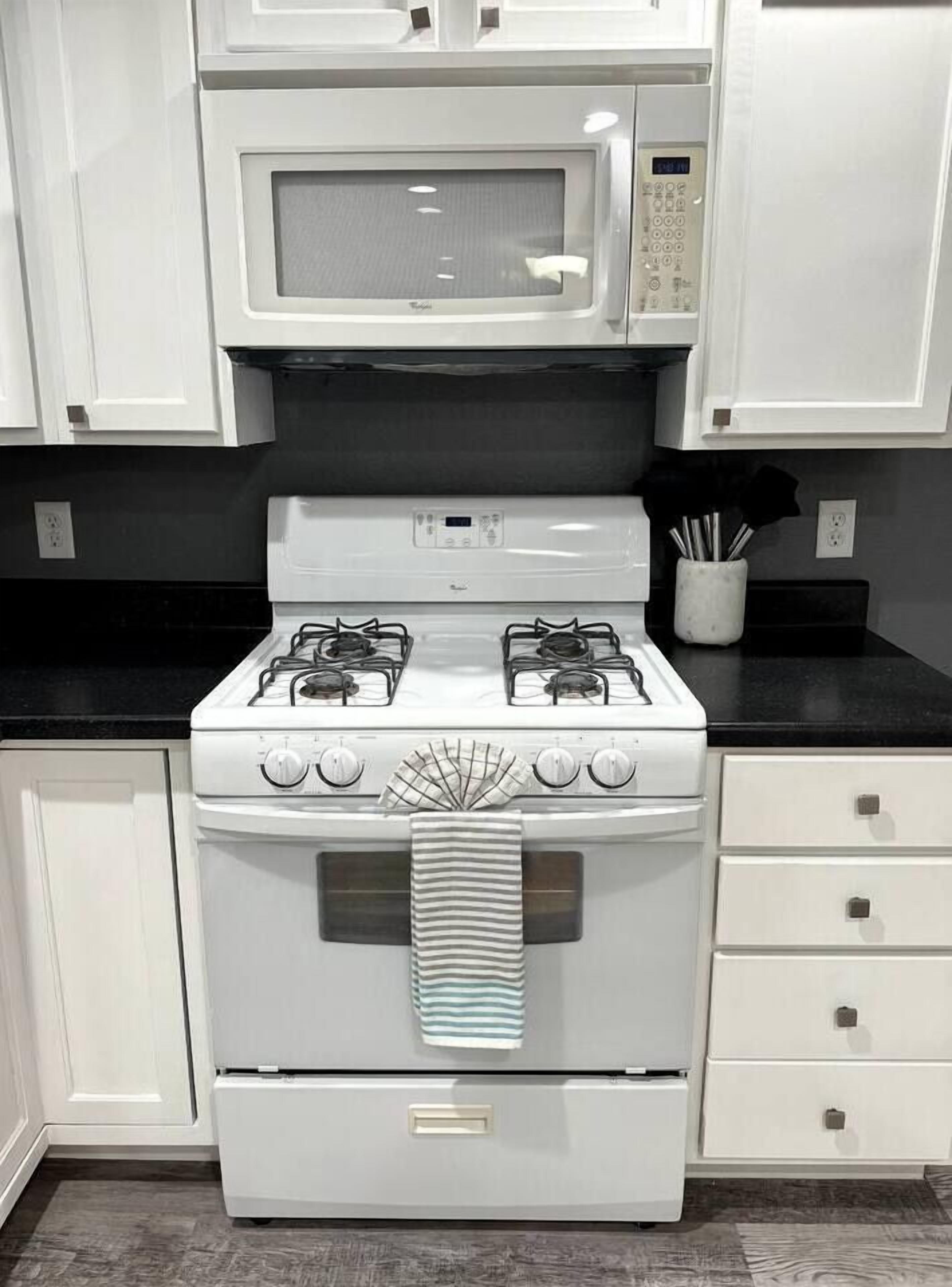 A kitchen with white cabinets, a microwave, a gas stove, and a striped towel hanging from the oven handle.