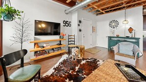 Un soggiorno moderno con soffitto in legno, TV a parete, tappeto in pelle di bovino e un armadietto color petrolio.