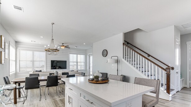 A spacious kitchen with a central island, a dining area with chairs, a staircase, and a living room with a TV. - Galveston Home w/ Decks + Views, Walk to Beaches! (Galveston)
