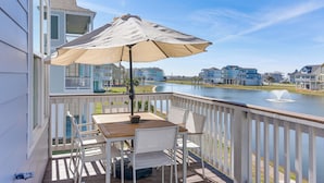A deck with a table and chairs, a beige umbrella, and a view of a lake and buildings. - Galveston Home w/ Decks + Views, Walk to Beaches! (Galveston)