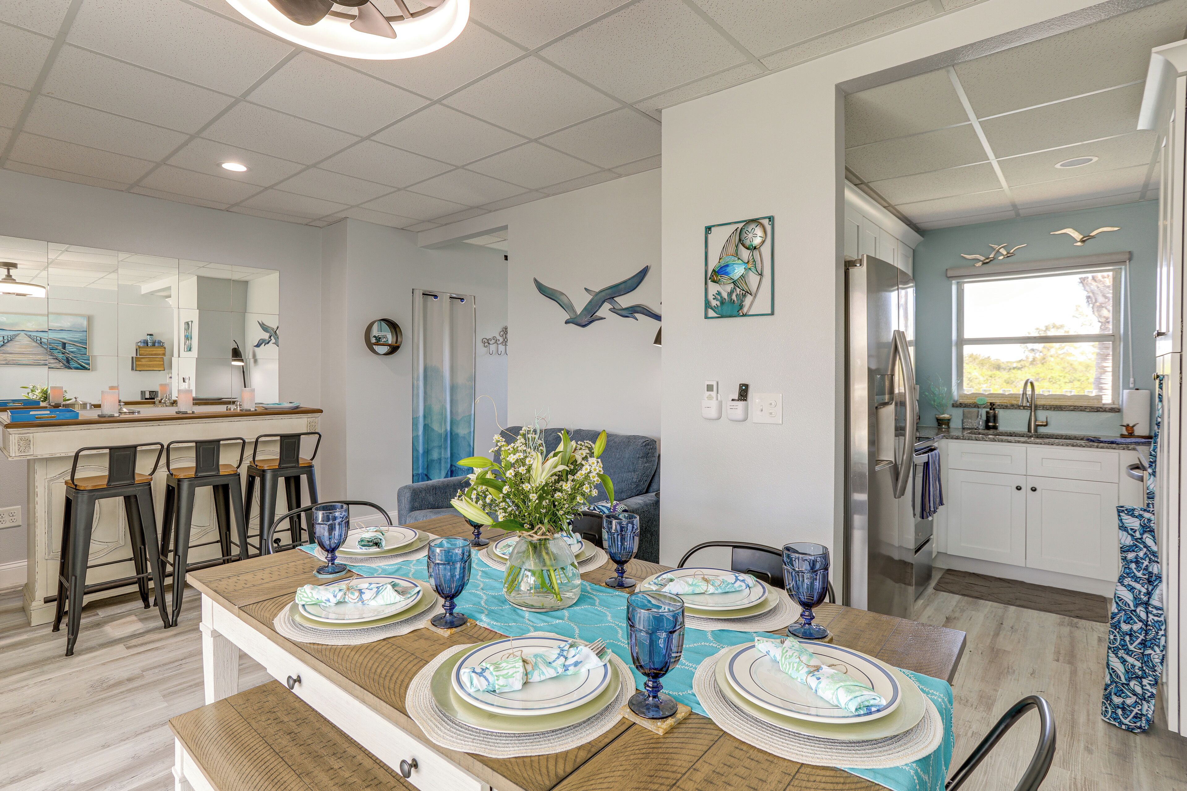A dining area with a wooden table set for four, a vase with flowers, and a view of the kitchen and living area.