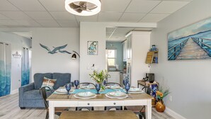 A dining area with a wooden table set for four, a blue sofa, and a ceiling fan. - Walk to Beach: Waterfront Indian Shores Condo (Indian Shores)