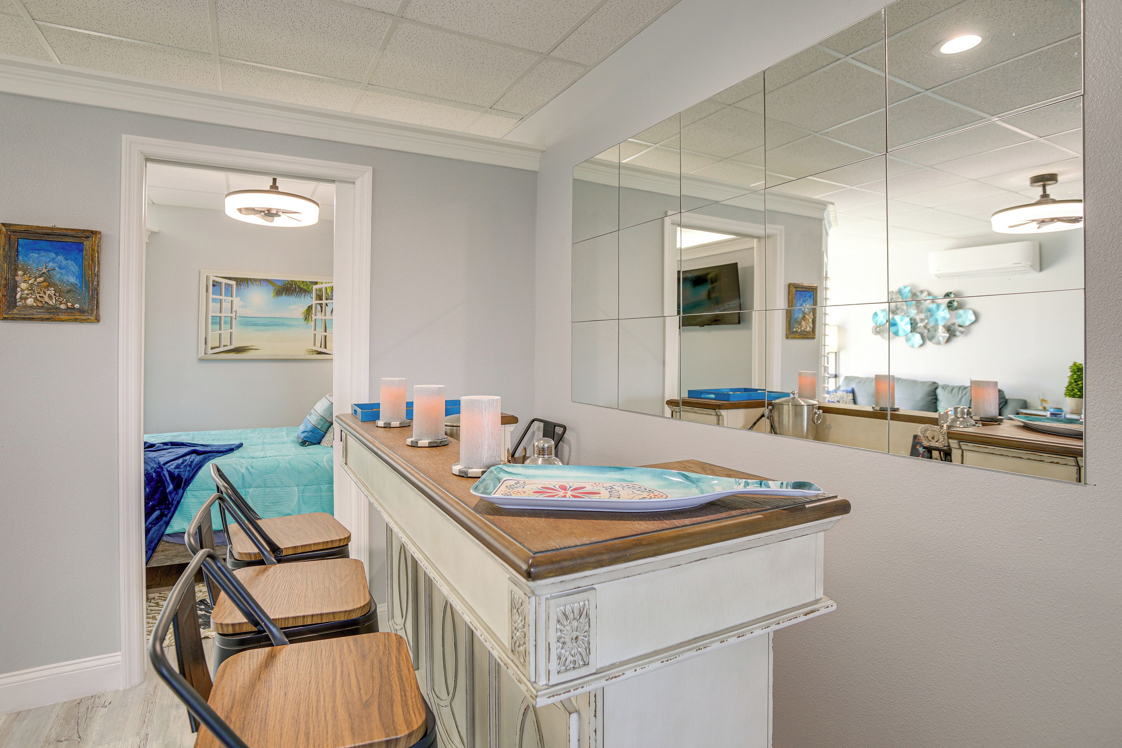 A hotel room with a bed, a desk with a chair, a mirror, and a view of the beach through an open window.