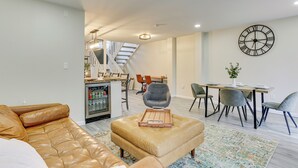 Una sala de estar moderna con un sofá de cuero, un comedor con mesa y sillas, y una escalera que conduce a otro nivel.